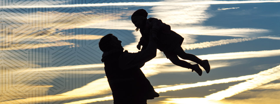 Ein Mann hebt ein Kind im Sonnenuntergang hoch. Die beiden sind nur als schwarze Silhouetten zu erkennen.